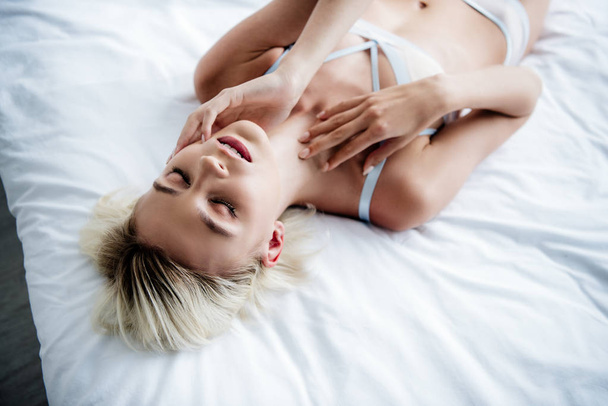 high angle view of attractive and blonde woman in white underwear lying on bed  - Fotografie, Obrázek