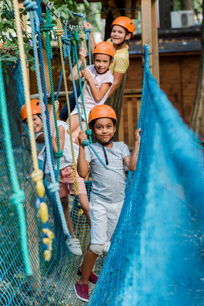 selective focus of cheerful multicultural kids in helmets near ropes  - Photo, Image