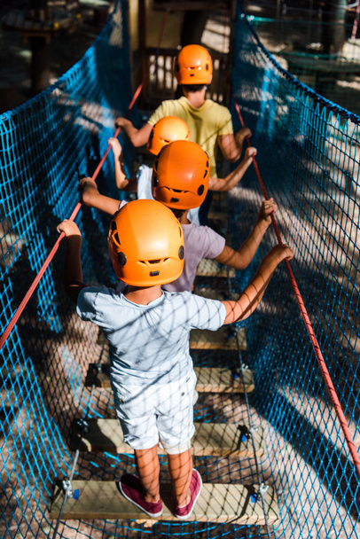 visão traseira de quatro crianças multiculturais em capacetes no parque de aventura
  - Foto, Imagem