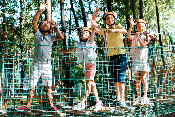 vrolijke multiculturele jongens in de buurt van vrienden in helmen zwaaien handen in adventure park  - Foto, afbeelding