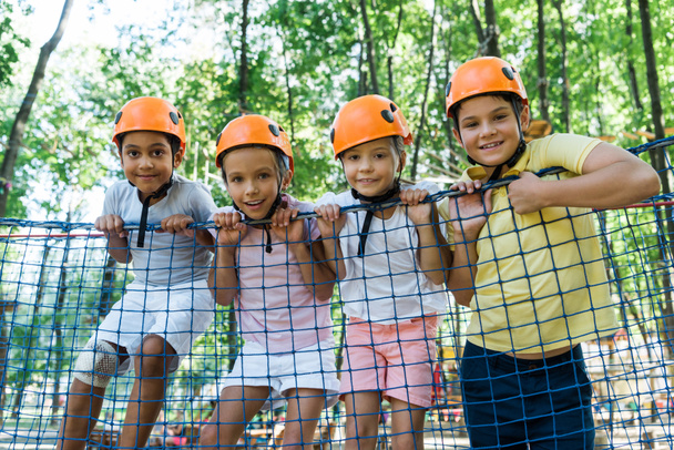 アドベンチャーパークの多文化少年の近くのオレンジヘルメットの子供たち  - 写真・画像