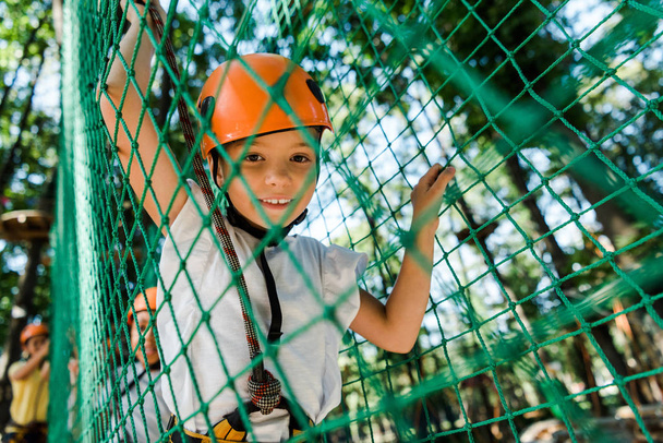 επιλεκτική εστίαση του χαρούμενος παιδί στο κράνος με εξοπλισμό ασφαλείας στο πάρκο περιπέτειας  - Φωτογραφία, εικόνα
