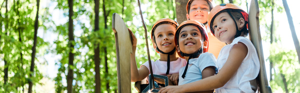 Panoramaaufnahme positiver multikultureller Kinder, die im Erlebnispark nach oben schauen  - Foto, Bild