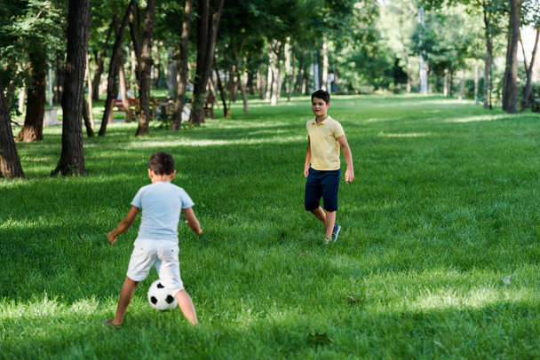 χαριτωμένα πολυπολιτισμικά αγόρια που παίζουν ποδόσφαιρο στο γρασίδι  - Φωτογραφία, εικόνα