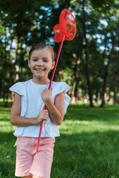 χαμογελαστό παιδί κρατώντας πεταλούδα δίχτυ στο πράσινο πάρκο  - Φωτογραφία, εικόνα