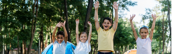 panoramic shot of happy multicultural kids with hands above heads  - Foto, immagini