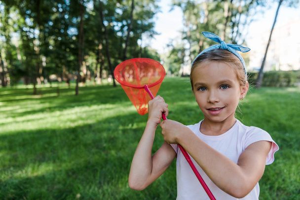 niño positivo sosteniendo red de mariposa en el parque verde
  - Foto, Imagen