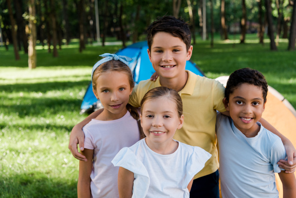 happy multicultural kids smiling near camps in park  - Foto, Bild