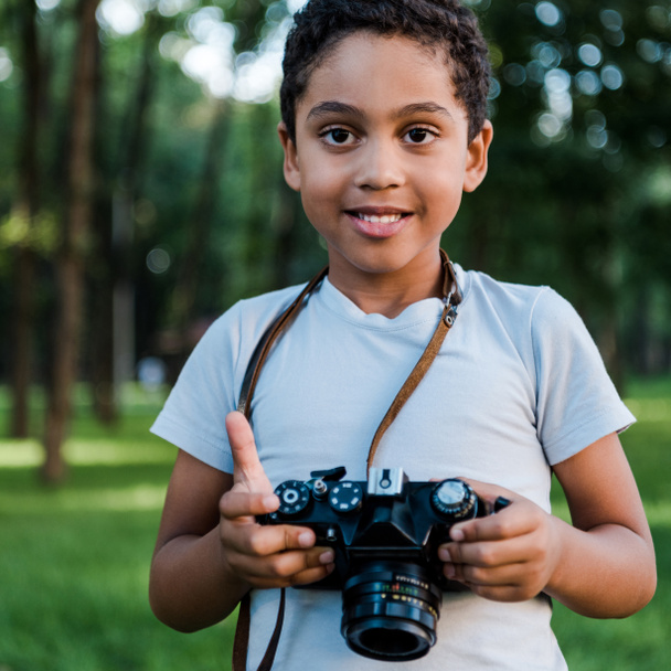 adorable african american boy holding digital camera in park  - Fotografie, Obrázek