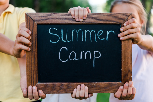 bijgesneden zicht op kinderen met krijtbord met zomerkamp letters  - Foto, afbeelding