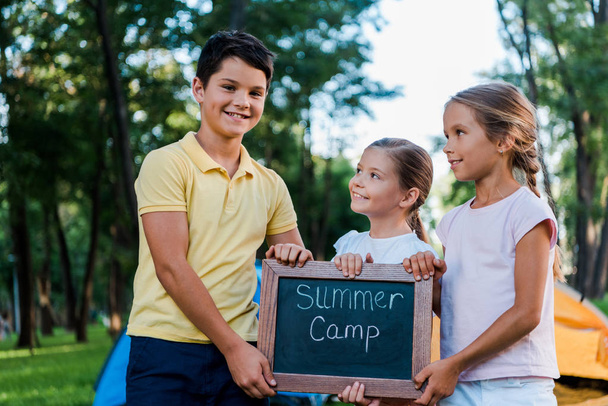 cheerful kids holding chalk board with summer camp letters  - 写真・画像