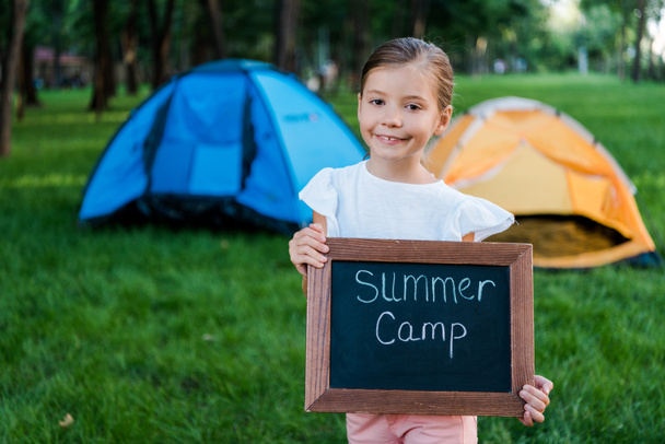 niño feliz sosteniendo pizarra con letras de campamento de verano
  - Foto, Imagen