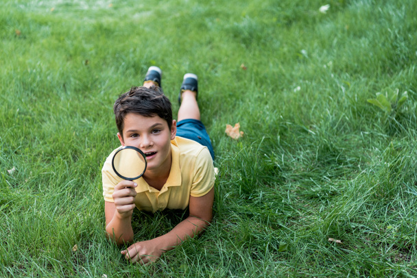 happy boy lying on grass and holding magnifier  - Photo, Image