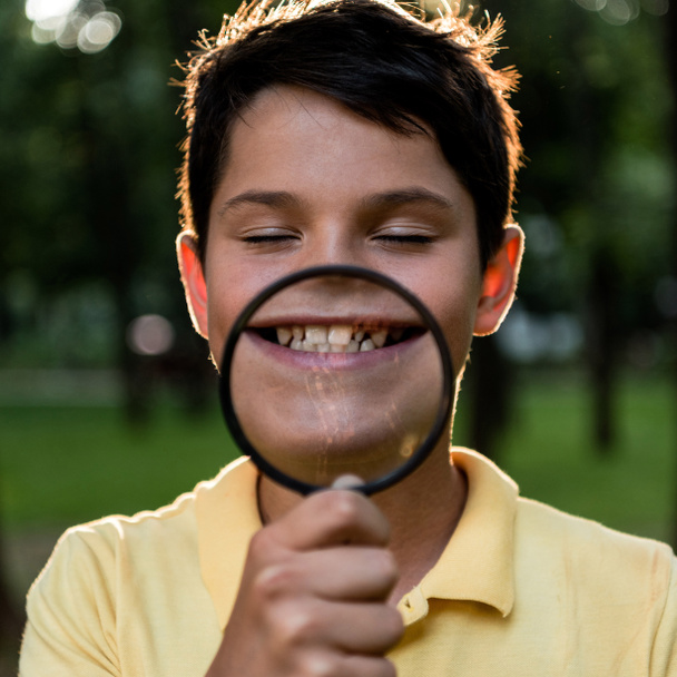 selective focus of cheerful boy holding magnifier near face  - Valokuva, kuva