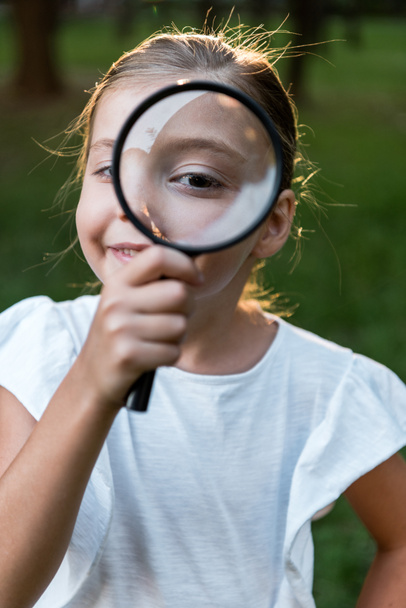 selective focus of cheerful kid holding magnifier near eye  - Фото, зображення