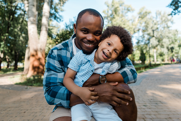 cheerful african american man hugging cute curly son  - Photo, Image