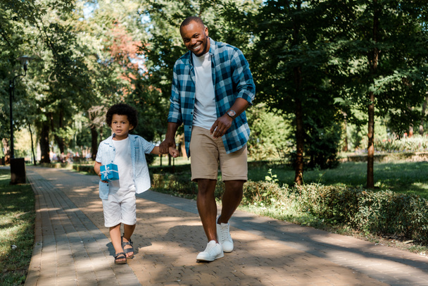 onnellinen afrikkalainen amerikkalainen isä kädestä poika kävellessään polulla puistossa
  - Valokuva, kuva