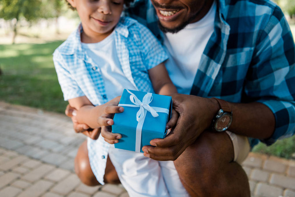 cropped view of happy of african american father and son holding blue gift box  - Zdjęcie, obraz