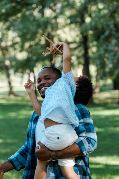 sorridente afro-americano homem segurando em braços bonito filho com brinquedo biplano
  - Foto, Imagem