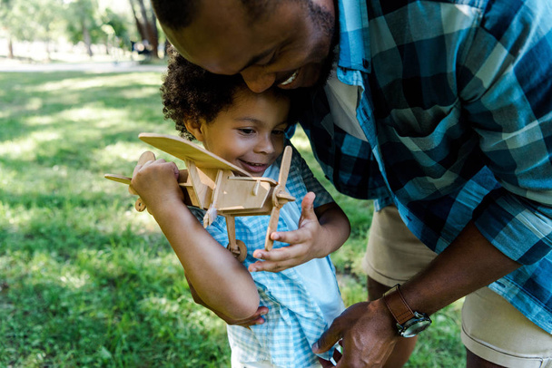feliz pai americano africano feliz perto bonito filho segurando biplano de brinquedo de madeira
  - Foto, Imagem