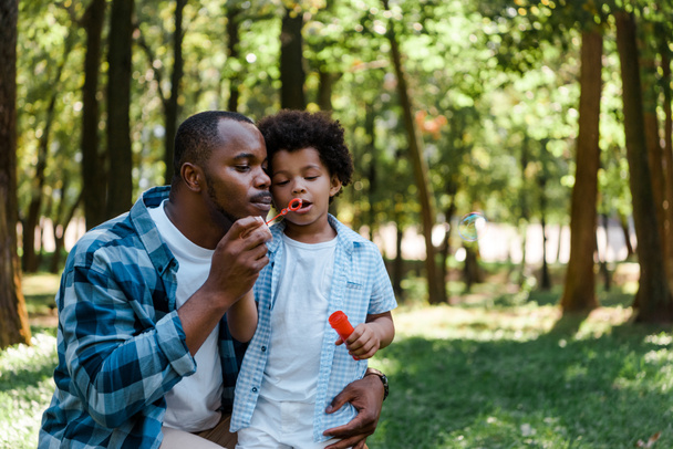 handsome african american father and cute son blowing soap bubble - Fotó, kép