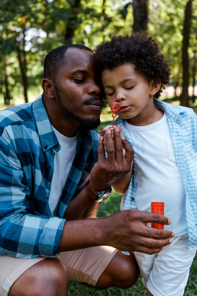 handsome african american father and curly son blowing soap bubble - Photo, Image