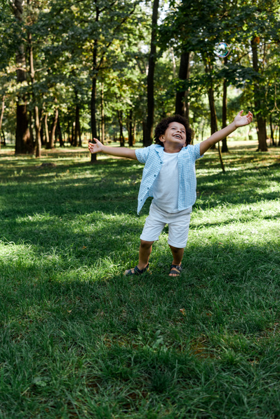 glückliches afrikanisch-amerikanisches Kind mit ausgestreckten Händen im Park  - Foto, Bild