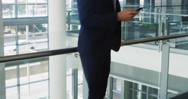 Front view of a young Caucasian businessman using a smartphone and laughing, standing in the lobby of a modern office building - Imágenes, Vídeo