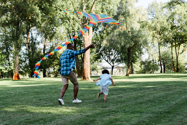 african american father holding kite near curly son in park - Фото, изображение