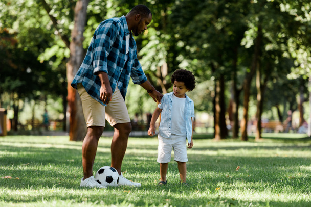 όμορφος Αφρικανός Αμερικανός πατέρας παίζοντας ποδόσφαιρο με χαριτωμένο γιο  - Φωτογραφία, εικόνα