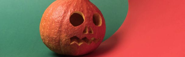 panoramic shot of spooky Halloween pumpkin on red and green background - Фото, изображение
