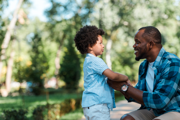 side view of cheerful african american father holding hands with son  - Foto, Imagem