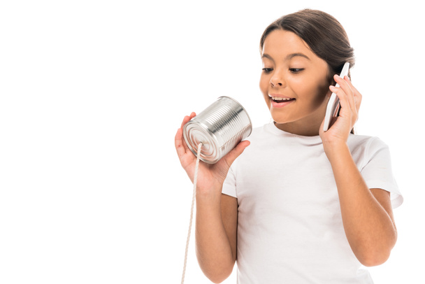 vrolijk kind praten op smartphone en spelen met tin kan geïsoleerd op wit - Foto, afbeelding