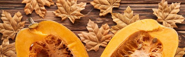 Panoramaaufnahme von Kürbishälften auf brauner Holzoberfläche mit getrockneten Herbstblättern - Foto, Bild