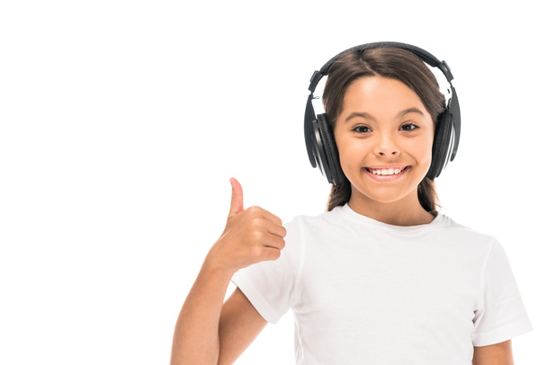 happy kid listening music in headphones and showing thumb up isolated on white  - Фото, изображение
