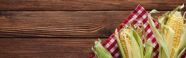 panoramic shot of raw corn on checkered tablecloth on wooden surface - Photo, Image