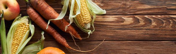 panoramic shot of fresh ripe apples, carrots and sweet corn on brown wooden surface with copy space - Foto, Bild