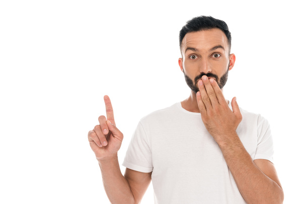 surprised man covering mouth and pointing with finger isolated on white  - Foto, afbeelding