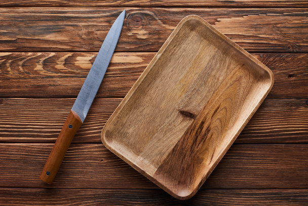 Widok z góry pustego prostokątnego naczynia w pobliżu noża na brązowej powierzchni drewnianej - Zdjęcie, obraz