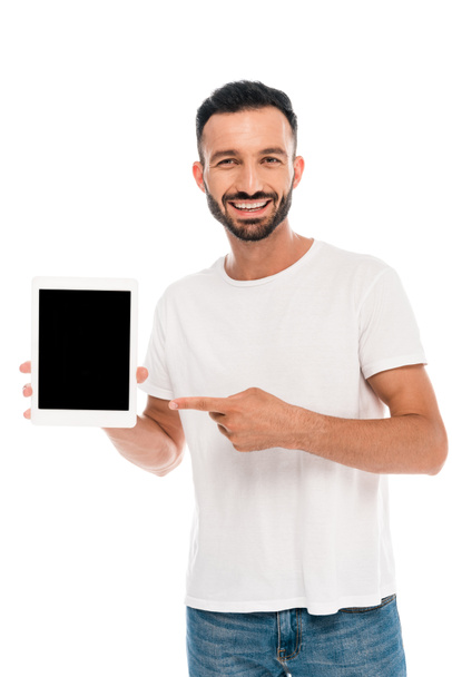 χαμογελαστός γενειοφόρος άνδρας που δείχνει με το δάχτυλο σε ψηφιακή ταμπλέτα με λευκή οθόνη απομονωμένη σε λευκό  - Φωτογραφία, εικόνα