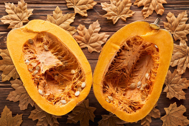 top view of ripe pumpkin halves on brown wooden surface with dry autumn leaves - Photo, image