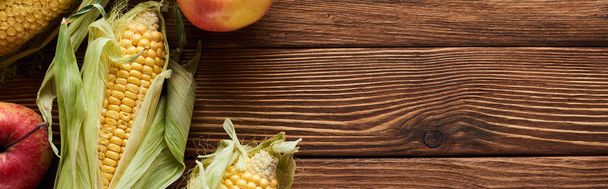 panoramic shot of fresh apples and sweet corn on brown wooden surface - Fotó, kép