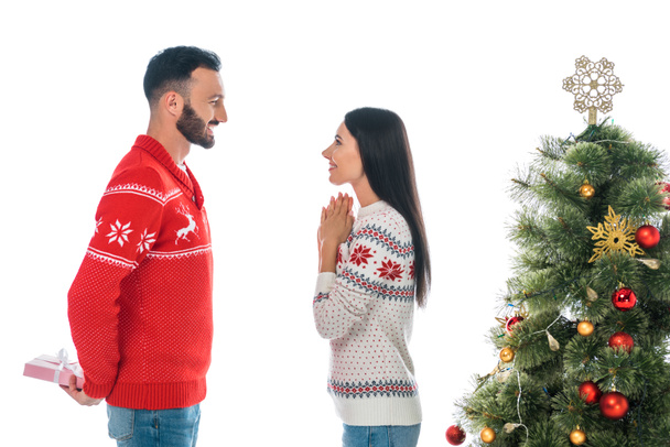 ευτυχισμένος γενειοφόρος άνδρας κρατώντας δώρο κοντά γυναίκα και χριστουγεννιάτικο δέντρο που απομονώνονται σε λευκό  - Φωτογραφία, εικόνα