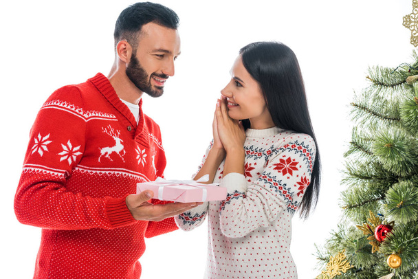hombre barbudo feliz sosteniendo regalo cerca de mujer alegre y árbol de Navidad aislado en blanco
  - Foto, Imagen