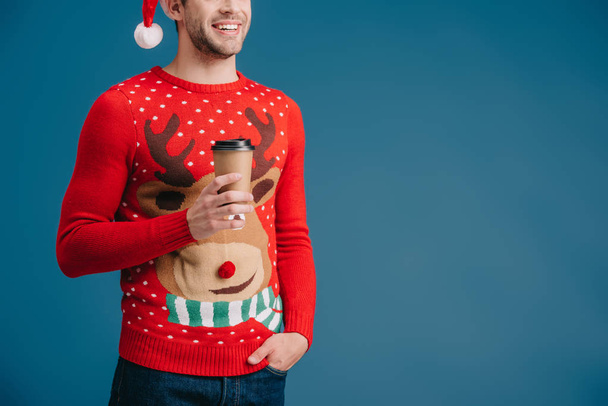 abgeschnittene Ansicht eines Mannes mit Weihnachtsmütze und Weihnachtspullover mit Kaffee to go auf blauem Grund - Foto, Bild