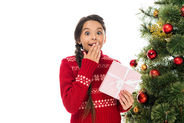 niño emocionado cubriendo la cara y sosteniendo regalo rosado cerca del árbol de Navidad aislado en blanco
  - Foto, Imagen
