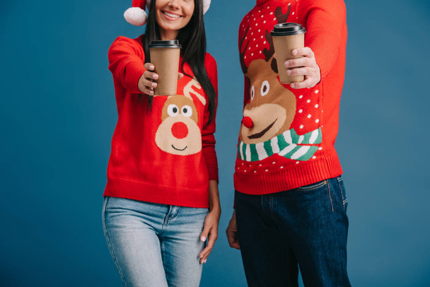 przycięte widok para w Christmas Swetry trzymając kawę, aby przejść izolowane na niebiesko - Zdjęcie, obraz