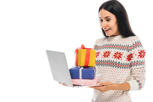 ευτυχισμένη γυναίκα σε πουλόβερ κρατώντας φορητό υπολογιστή με δώρα που απομονώνονται σε λευκό  - Φωτογραφία, εικόνα