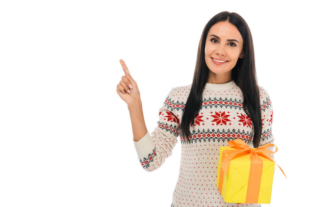 cheerful woman in sweater holding present and pointing with finger isolated on white  - Foto, imagen