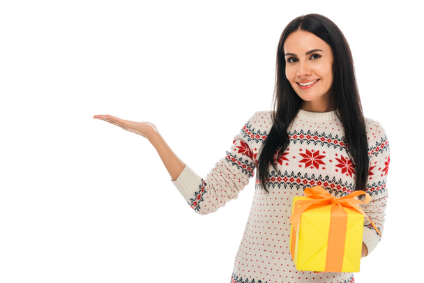 cheerful woman in sweater holding gift box and pointing with hand isolated on white  - Фото, зображення